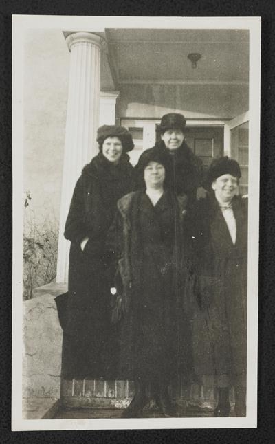 Cora Wilson Stewart and three unidentified females, all standing in front of a house and wearing long coats and hats