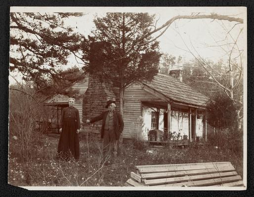 Log cabin with unidentified couple standing outfront