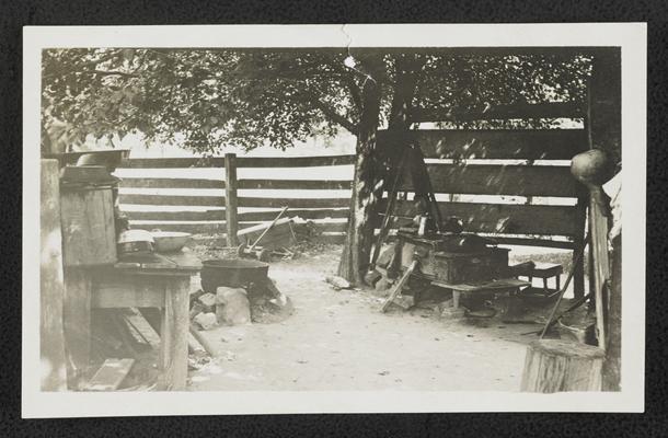 Fenced outdoor spaced with household items, back of the photograph reads: Living out in the open