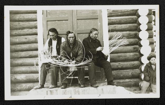 Three men weaving baskets, a young boy stands off to the side. Back of the photograph identifies them as: 1. John Little Blaze 2. No Coat 3. Sure Chief