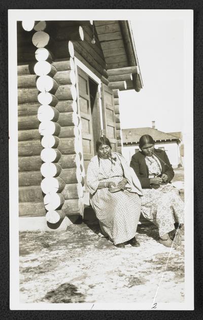 Two women sitting, smoking pipes, and weaving baskets. Back of the photograph identifies them as: 1. Strikes First 2. Mrs. Redfox