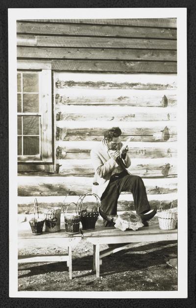 A man taking notes, leg propped up on the same display table from item #589. Back of the photograph identifies him as: Takes Gun on Top