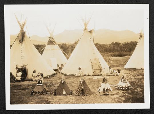 Women and children in traditional dress, sitting in front of teepees. Back of the photograph reads: Indiana teepees and miniature teepees for the children