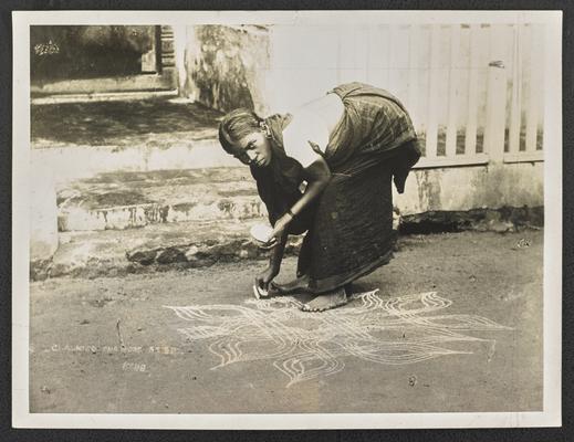 An African American woman bending over, drawing a chalk design on the concrete