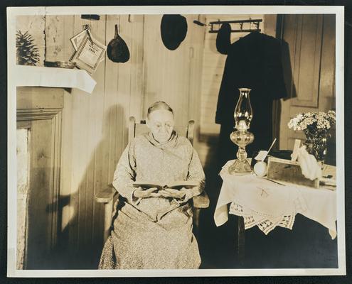 Female, unidentified, sitting in a chair and reading a book. Back of the photograph reads: N.C. sent by S.L. Davis