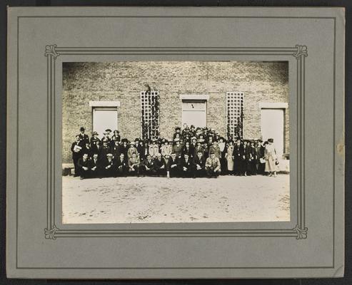 Group photograph of adult men and women, standing in front of a brick building, Cora Wilson Stewart standing on the right hand side