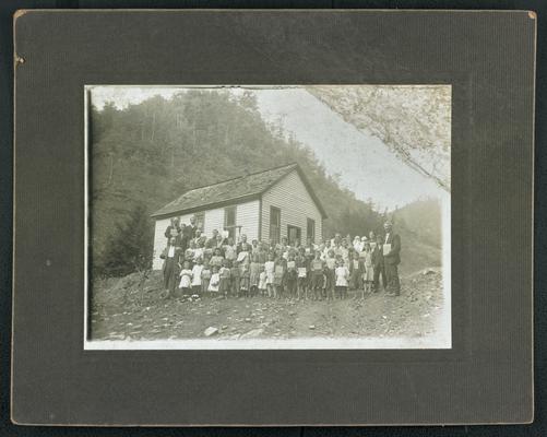 Unidentified students, holding books and standing in front of the school house