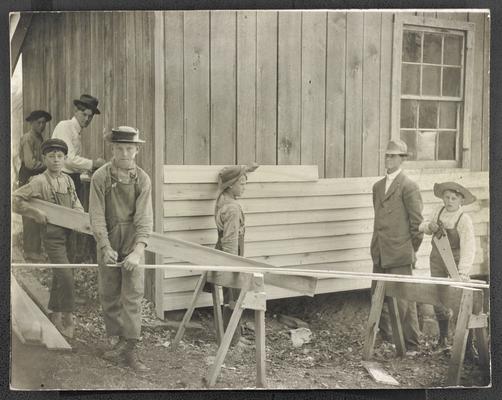 Unidentified male students, sawing wood and nailing panels on the school house