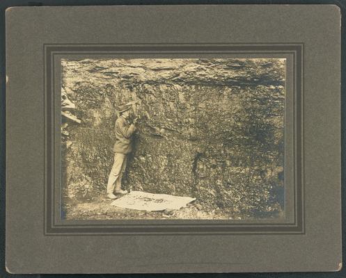 An unidentified man taking an iron to coal. The back of the photograph reads: The Mountain Child- His environment
