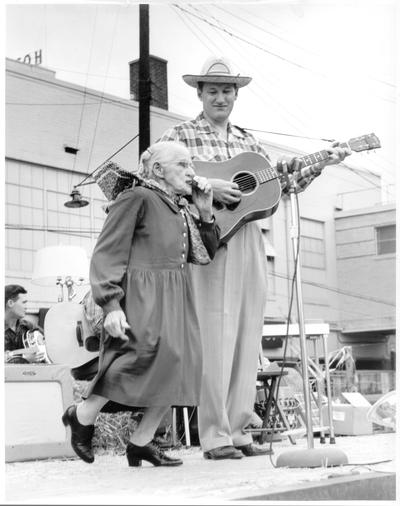 Adults; In Costume; Man in straw hat plays guitar, elderly woman plays harmonica