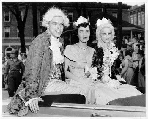 Adults; In Costume; One male and two females riding in convertible at a parade