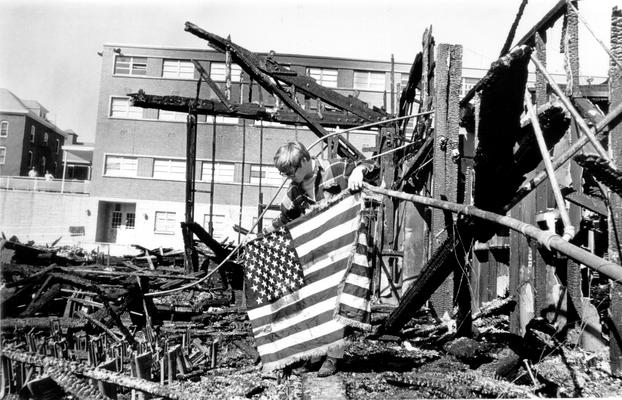 House Fires; A man holds the American Flag in front of a burnt building