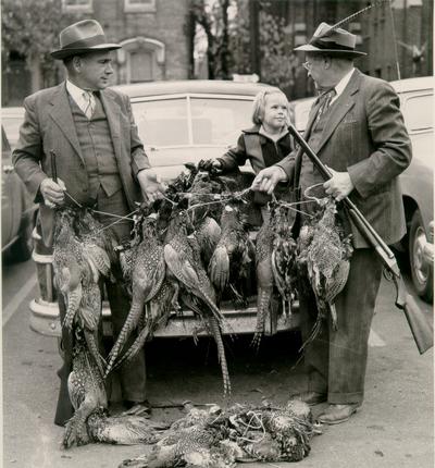 Animals; Miscellaneous; Two well-dressed pheasant hunters show their killings to a little girl