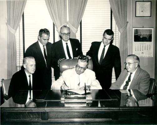 Men; Groups; Unidentified; Five men watch as one signs an important document