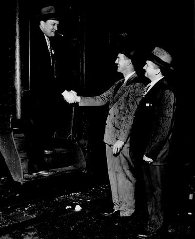 Men; Groups; Unidentified; Two men stand in the rain to greet a friend stepping off the train