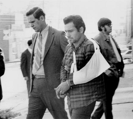 News Photographs; Police escort a man with his arm in a sling