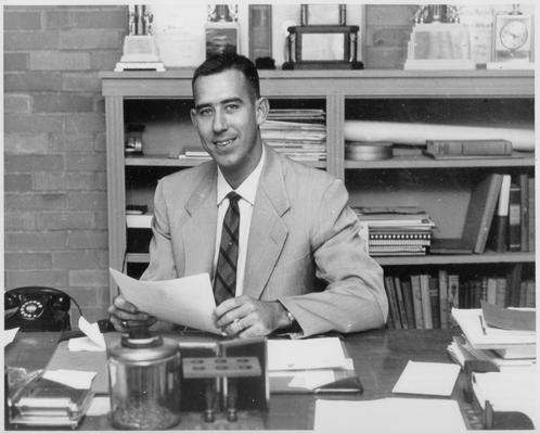 Newton, C. M.; A smiling Newton sitting behind his office desk