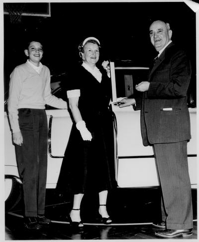 Rupp, Adolph F.; Rupp stands beside a woman and a boy with a car behind