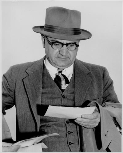 Rupp, Adolph F.; Rupp wears a pair of glasses looking on a piece a paper