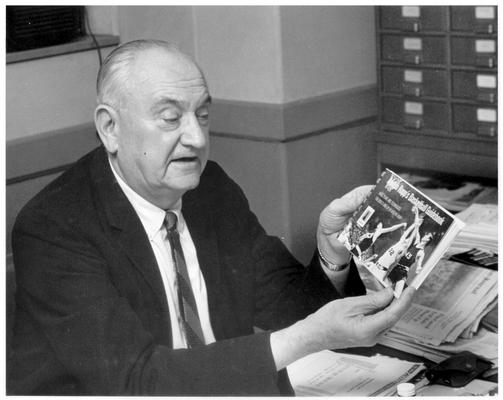 Rupp, Adolph F.; Rupp holds a book titled 
