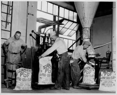 Schenley Distillers, Inc; Three men lifting sacks in a factory