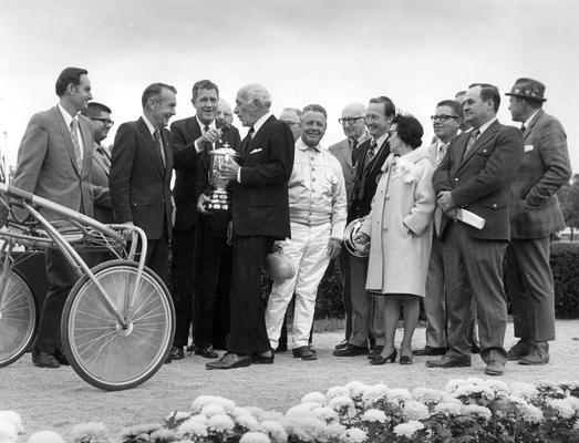 Horses; Harness Racing; Winner's Circle; A man hold the trophy is being interviewed in the crowd