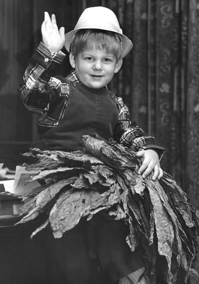 Tobacco; A child waves for the camera, holding a sheaf of tobacco