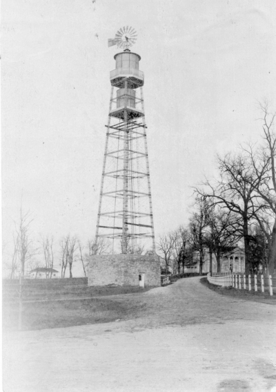 Exterior view of a water tower with tank and windmill on top. Silver Print