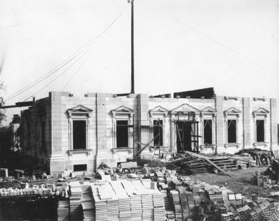 Exterior of Elmendorf Farm Mansion; the stone walls of the first floor are up, building is under construction, materials are stacked in front of the building. Silver Print