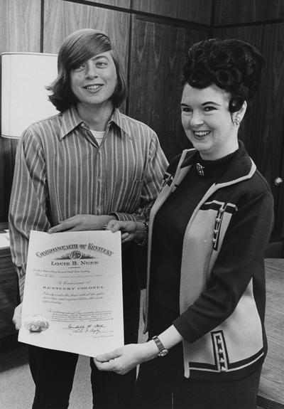 Adams, Jon, University of Kentucky Freshman is presented with certificate signifying that he is commissioned as a Kentucky Colonel; he and three other students helped Dotty Priddy (right, presenting the certificate) fix a flat tire, and is presented with this honor as recognition of his kindness; Dotty Priddy was a representative to the Kentucky General Assembly from Louisville, photographer: Public Relations Department