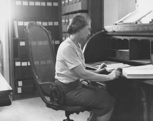 Cooper, Mary Hester, born 1904, died 1987, University Archivist 1956 - 1970, pictured seated at University President James K. Patterson's desk looking over biographies of Patterson, Public Relations Department