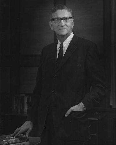 Kirwan, Albert, University of Kentucky President from 1968-1969, standing with right hand on books and left hand in pocket