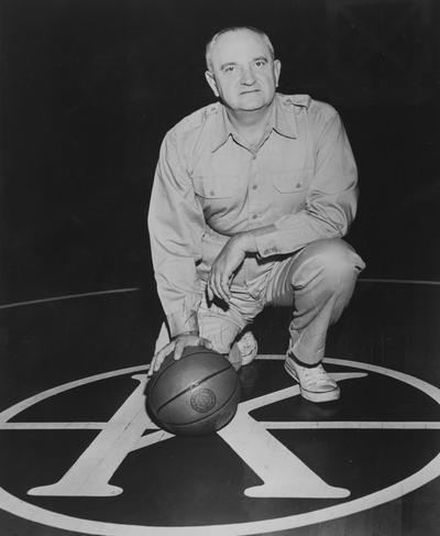 Rupp, Adolph, University of Kentucky Basketball Coach 1930-1971, signed print of Rupp, posing with basketball at center court at Memorial Colleseum, note reads 