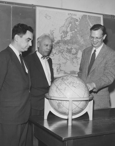 Vandenbosch, Amry, pictured looking at a globe with 2 other men, in center