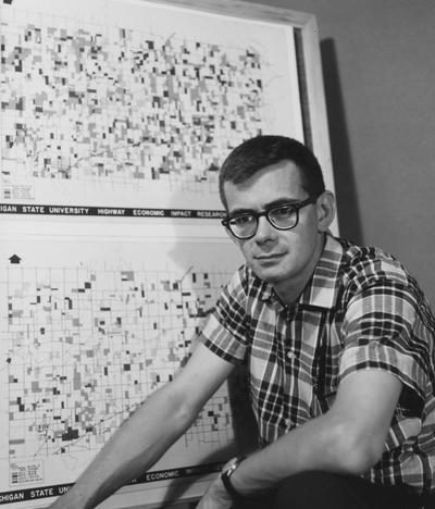 Vargha, Louis Andrew, pictured in front of maps at Michigan State University