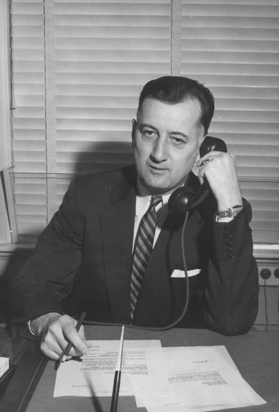 Wild, Raymond W., Director of Public Relations, pictured sitting at desk