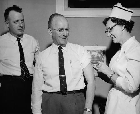 Chamberlain, Leo M., Professor, Education, University Vice President, pictured receiving inoculation from Henrietta Frazier at the UK Infirmary in preparation for trip to Indonesia, Also pictured is William M. Jenkins, Jr., Assistant Coordinator for Indonesian Projects, Public Relations Department photograph, Featured in April 23, 1958 Lexington Herald