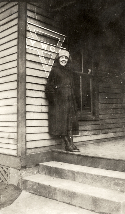 A portrait of an unidentified woman standing on the steps of a Y. M. C. A. (Young Women's Christian Association) residence. This print was found pasted to the back of page 115 of 