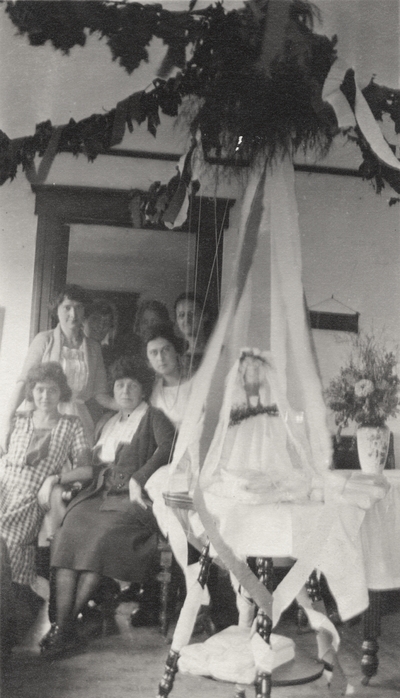 A group portrait of unidentified women inside a house that has been decorated for some occasion. This print was printed by the Elizabeth Novelty Co. 923 Elizabeth, N. J. This print was found among the 