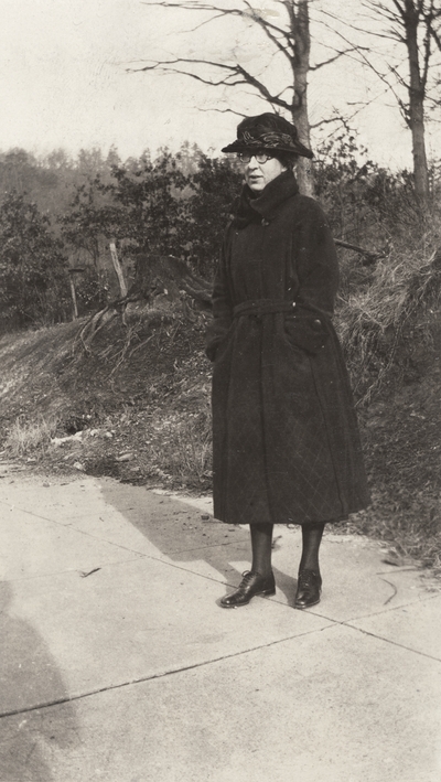 A portrait of an unidentified woman standing on a sidewalk. This print was found pasted to the front of page 116 of 