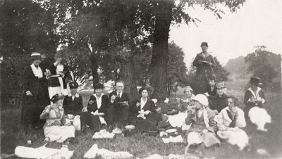 A group portrait of people having a picnic outdoors. This print was found pasted to the back of page 107 of 
