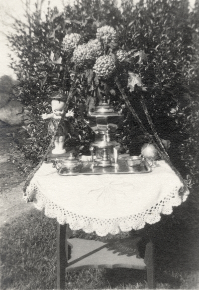 An image of a table outside decorated with flowers and doll. This print was found among the pages of 
