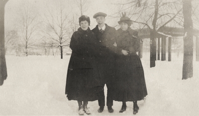 A portrait of two unidentified women and a man standing outside in snow. This print was found pasted to the front of page 105 of 