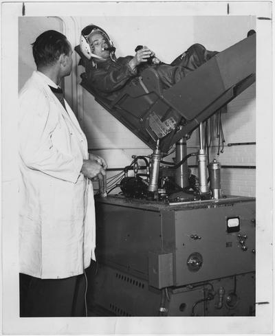 Dr. Charles Wilson of the AeroMedical Research Laboratory at Wright Air Development Center in Dayton, Ohio, tests a chair designed to simulate the vibrations of space travel; Dr. R. R. Coermann chief engineer for vibration study, watches Wilson