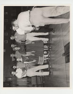 Sergeant Perkins demonstrates the proper bowling swing for Ed Beck; Also looking on from left are: Harold Ross, Hickman; Ed Couch, Owensboro; Darlene Wylie, Lexington; Vernon Hatton, Lexington; Pat Alexander, Lexington; John Crigler, Burlington; and Adraian Smith, Kirksey