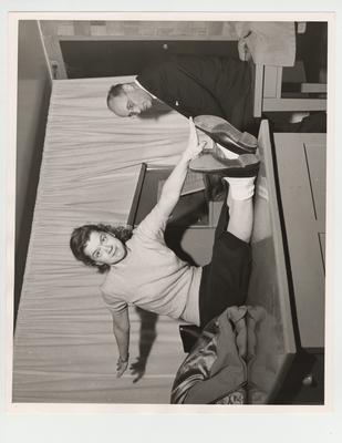 A woman touches her toes as Dr. Ernst Jokl, director of Rehabilitation Center, watches