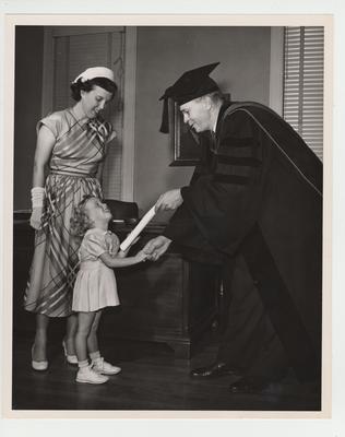 Dean C. C. Carpenter hands a diploma to a little girl; Photographer: Spengler Studio