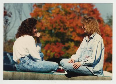 Two female students talk during a break; Fall foliage in background