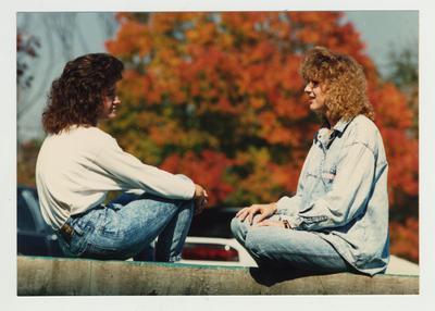 Two female students talk during a break; Fall foliage in background