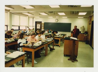 A male professor teaches while students listen